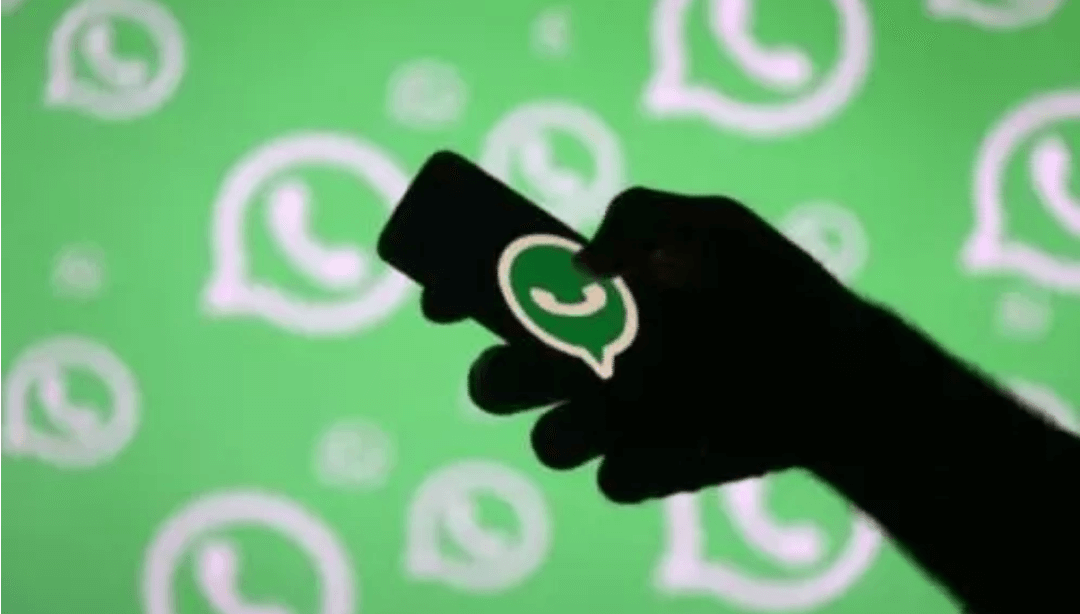 Siluet tangan memegang smartphone dengan logo WhatsApp di layar